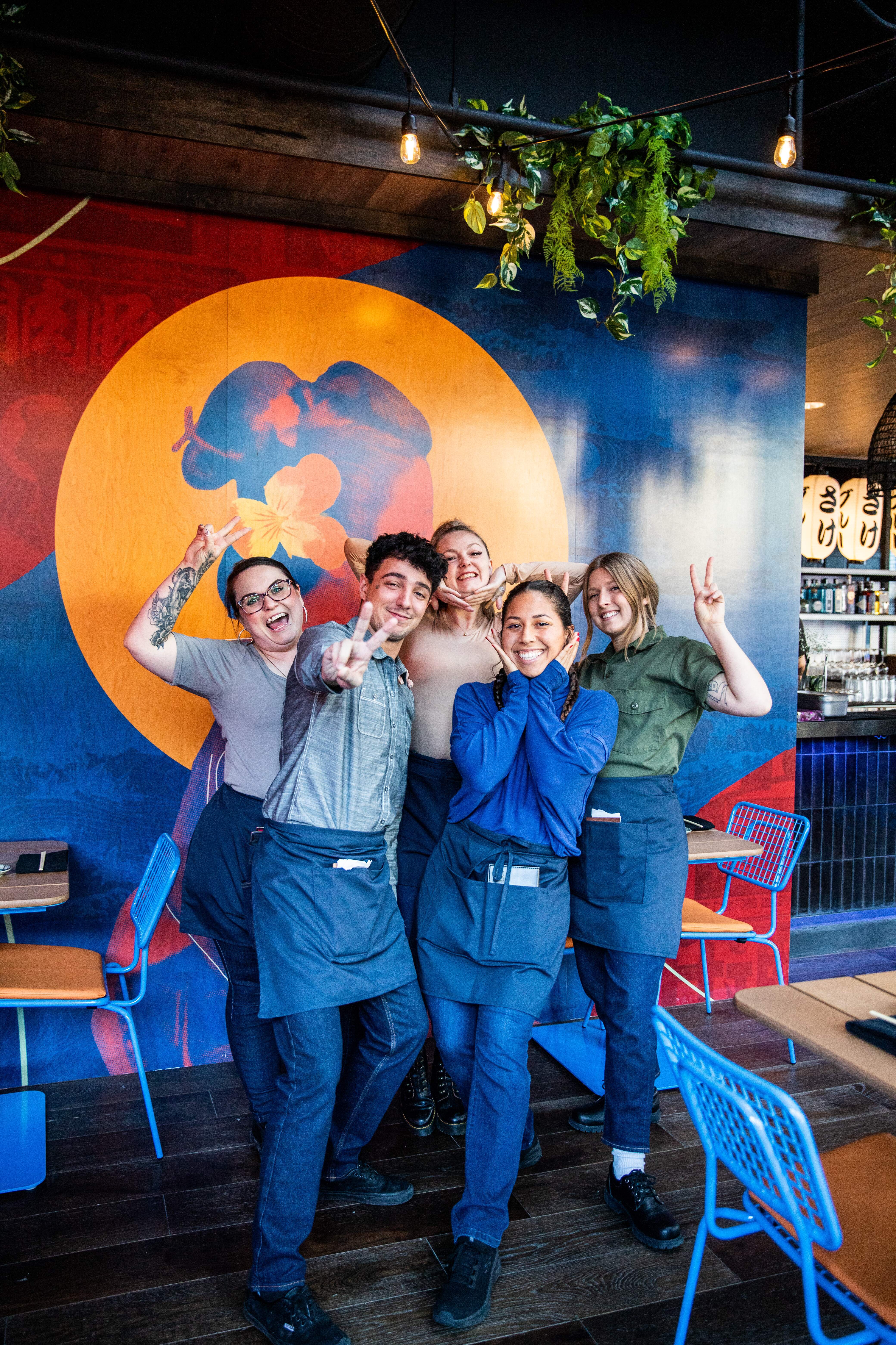 Blue Sushi Sake Grill team smiling in front of colorful mural for group picture.