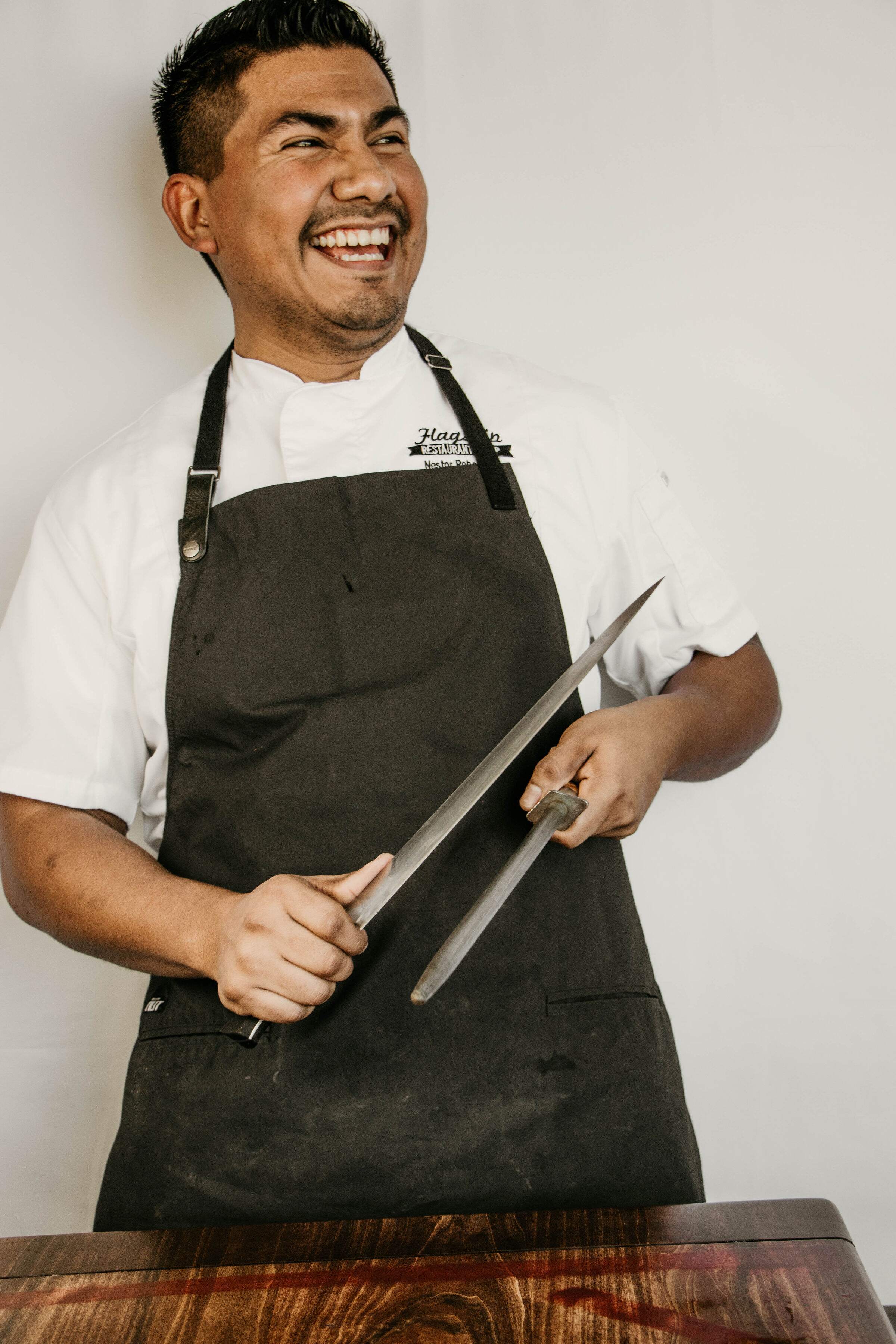 Chef at Blue Sushi Sake Grill in black apron, happily holding a knife.