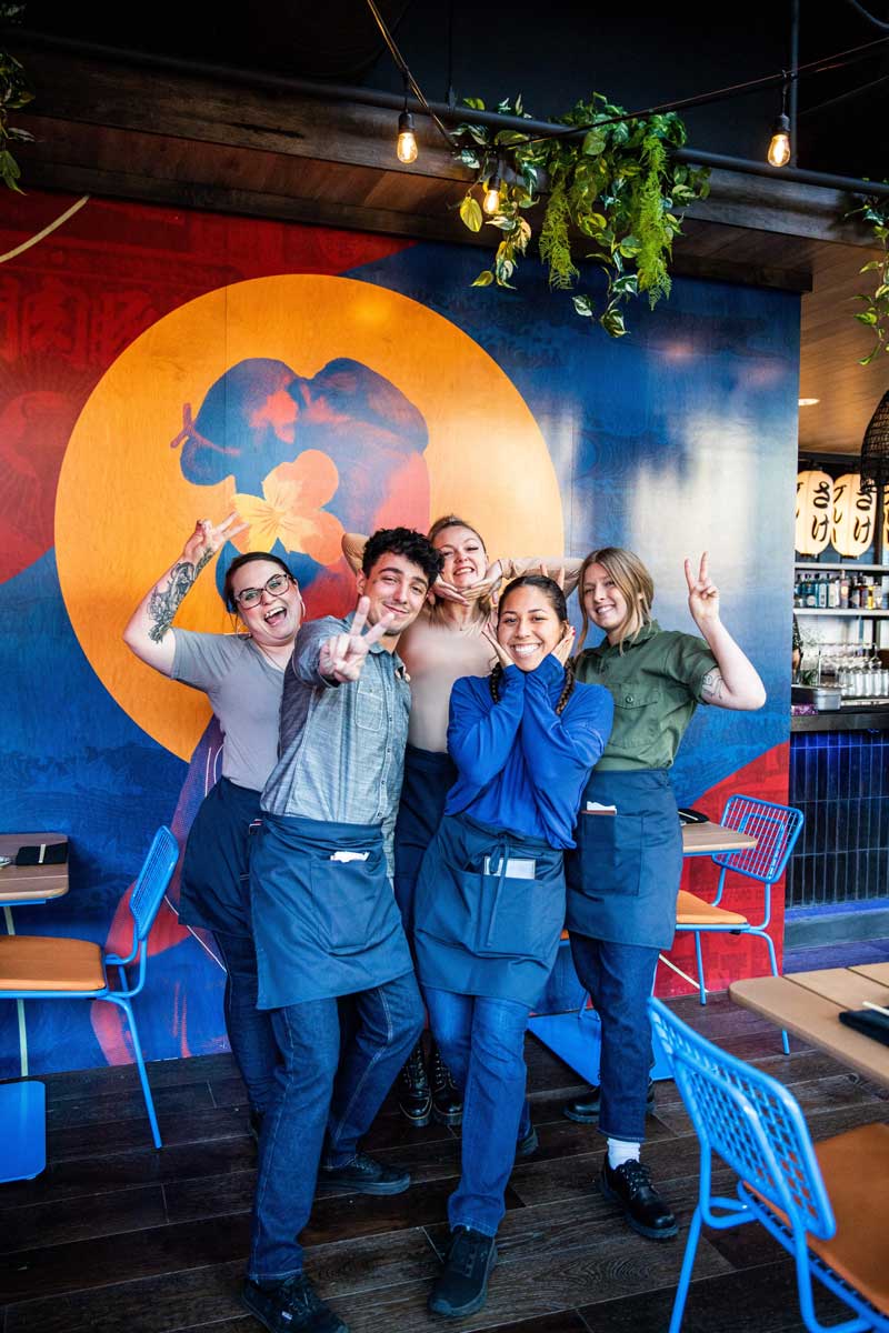 Blue Sushi Sake Grill team smiling in front of colorful mural for group picture.