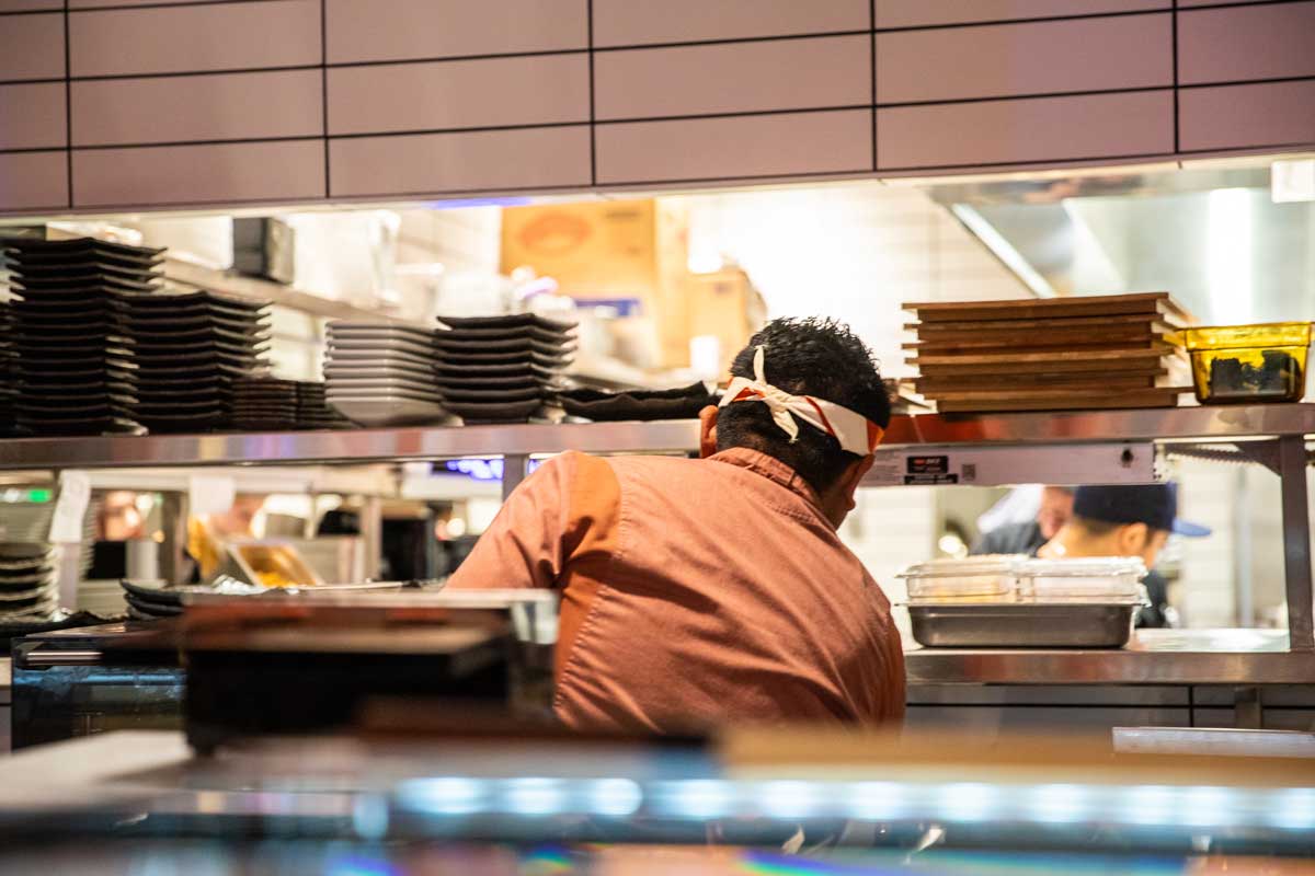 Blue Sushi chef working in the kitchen handing out food. 