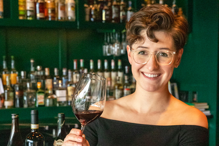 A wine sommelier holding a glass of red wine, examining its color and aroma.